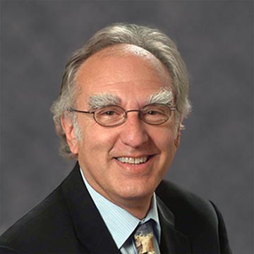 Smiling man wearing glasses and a suit against a grey background.