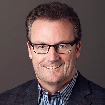 A person wearing glasses and a suit against a dark background.