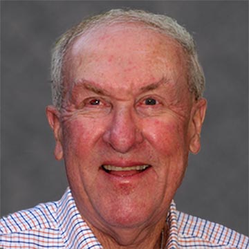 A man smiling in front of a grey background.