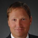 A person in a suit against a dark background.