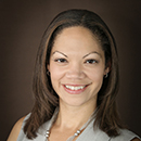 A woman smiling against a dark background.