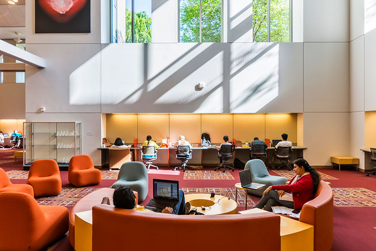 Library interior with seating, computers, large windows, and shelves.