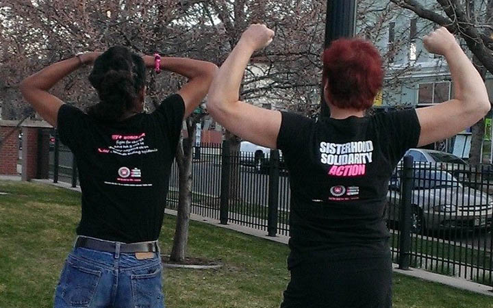 Two people flexing in 'Positive Women Network USA' T-shirts outdoors.
