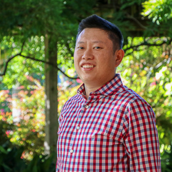 A person in a red checkered shirt smiling outdoors.
