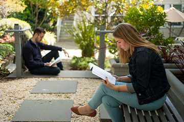 Two students reading on benches in an outdoor garden.