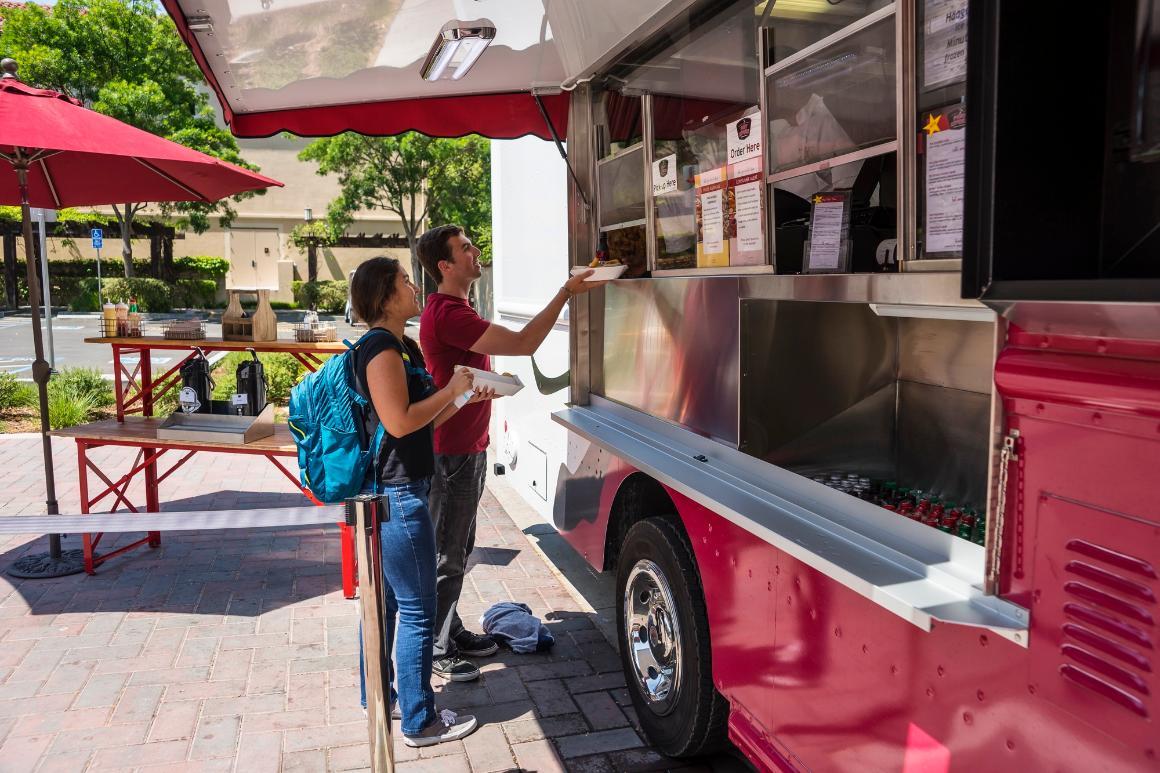 Two people order food from a red food truck on campus.