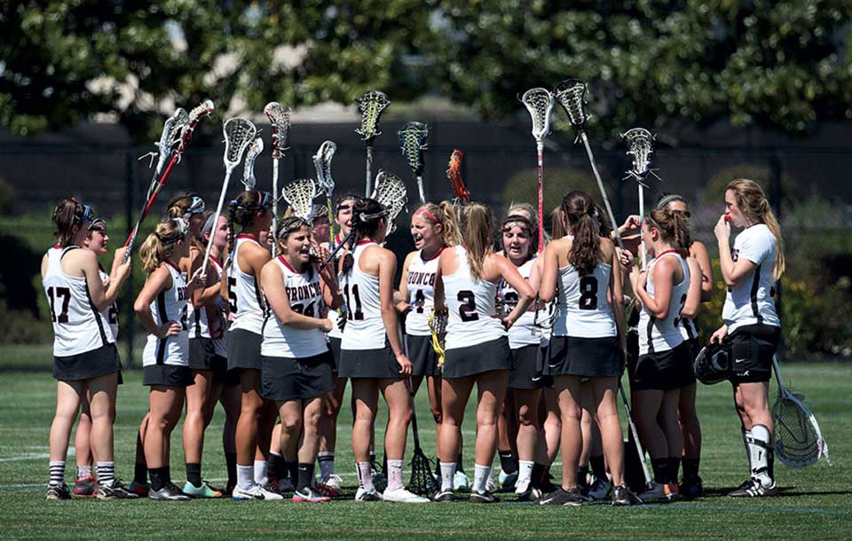 Women's lacrosse team huddled together on a field.