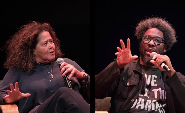 Two people onstage speaking, gesturing with their hands, holding microphones.