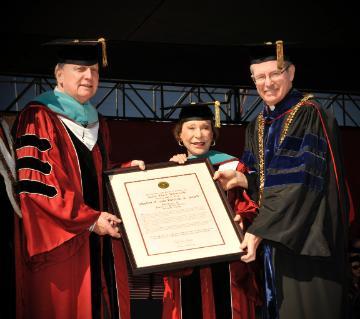 Schotts in graduation robes receiving their honorary degree from Fr. Engh 