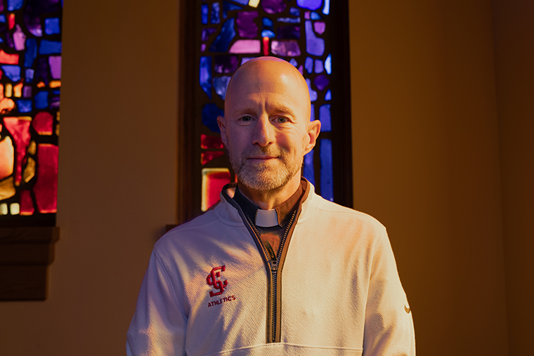 Fr. Carnes standing in front of stained glass at Jesuit Residences