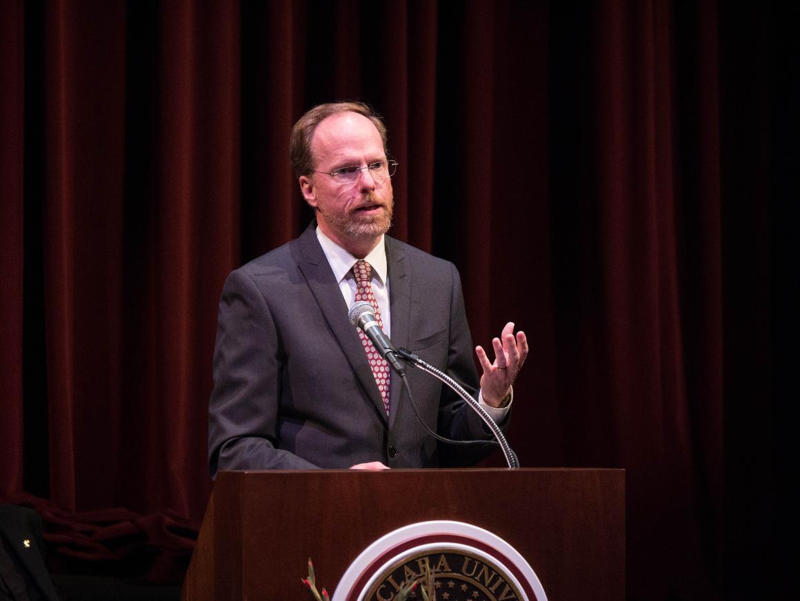 Man giving a speech behind a podium with a university seal. image link to story