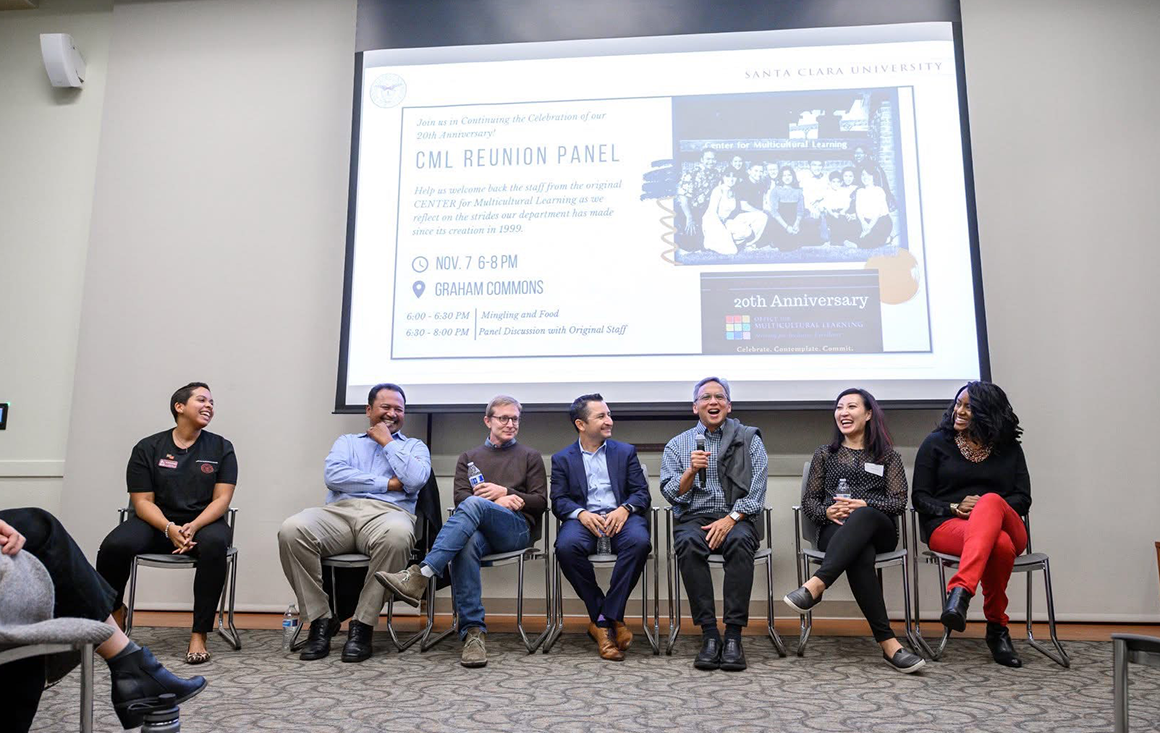 A panel of older individuals sit in a row in front of a projected image of the same people years ago.