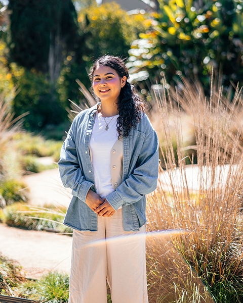 A young Latina woman stands in a grassy garden.