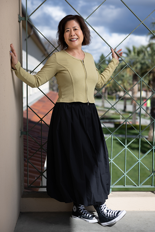 A woman poses on a cement alcove with ornate metal bars, showcasing her sneakers.