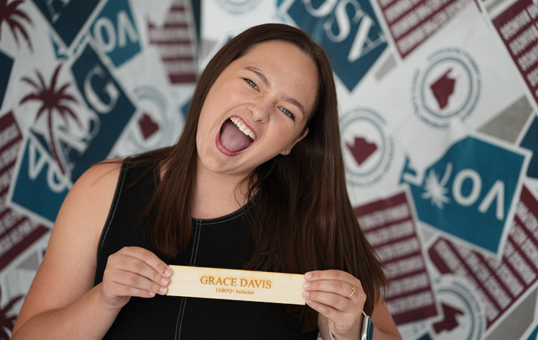 A young woman with a wide cheering smile holds her senator placard which says 