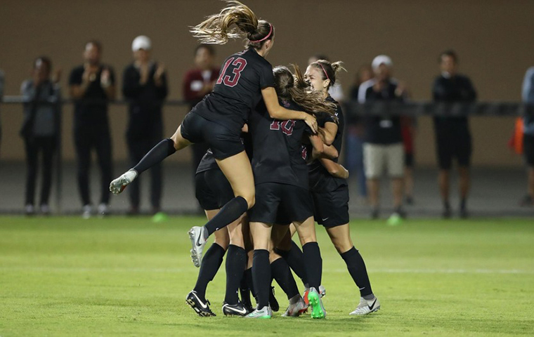 Women's soccer team celebrate in a circle.