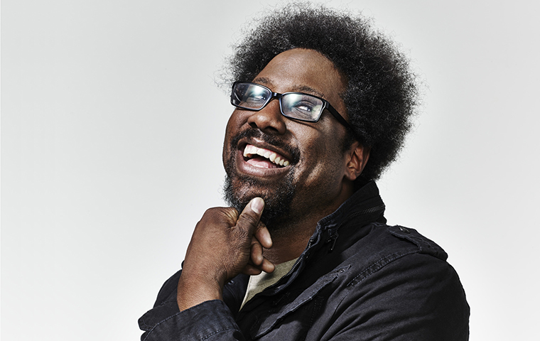 W. Kamau Bell smiling with his hand on his chin.