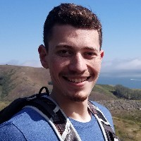 Smiling person outdoors with mountains and sky in the background.