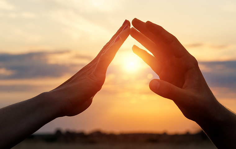 Two hands reaching for each other in front of a setting son