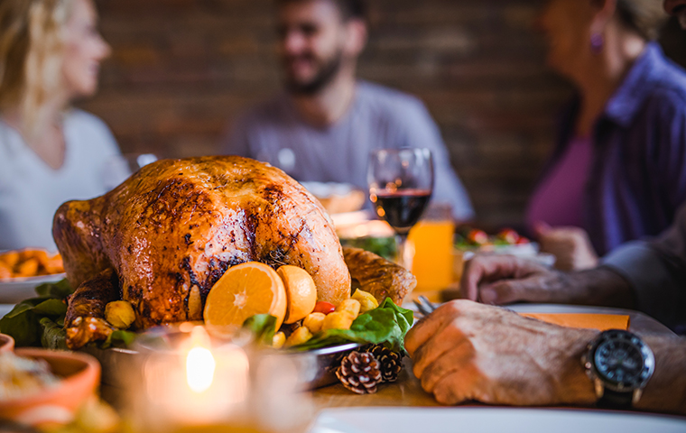 People enjoying Thanksgiving dinner with a turkey centerpiece on the table.