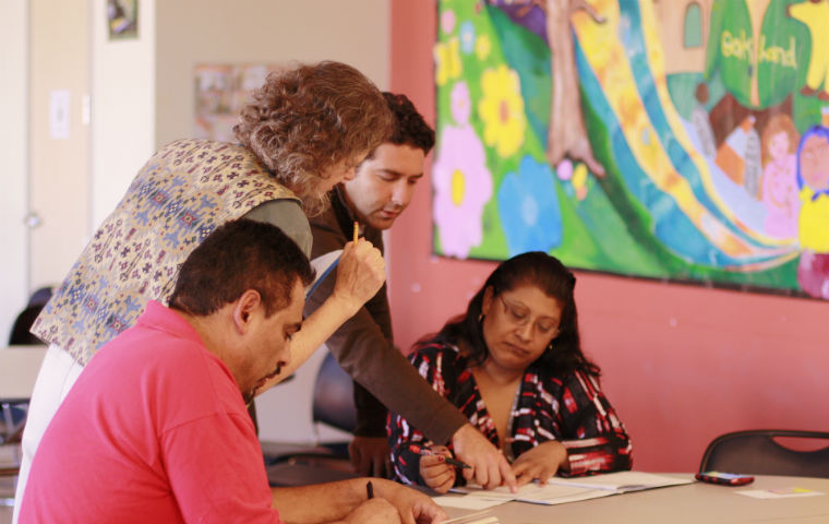 Four people looking at papers on a table, in front of colorful art.