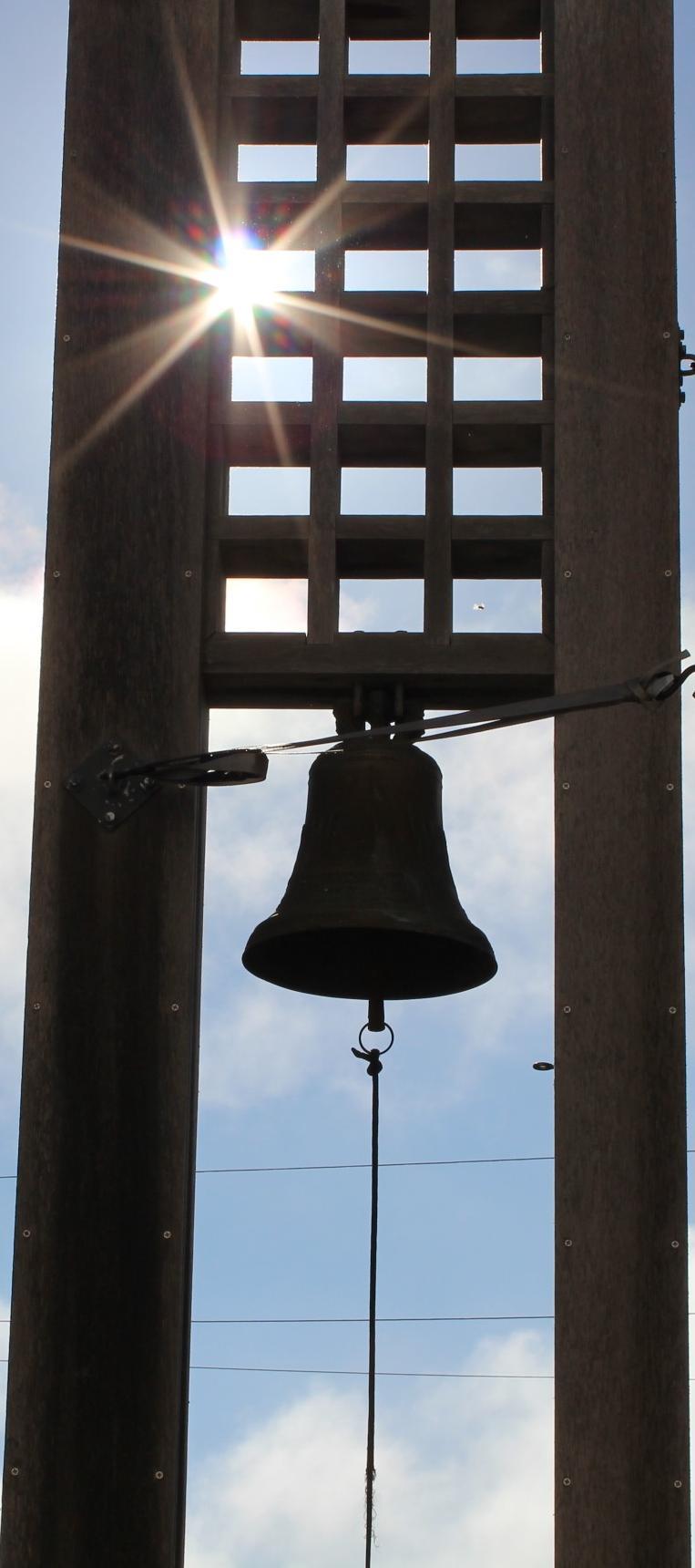 A bell hanging from a tall structure with a sunny sky background.