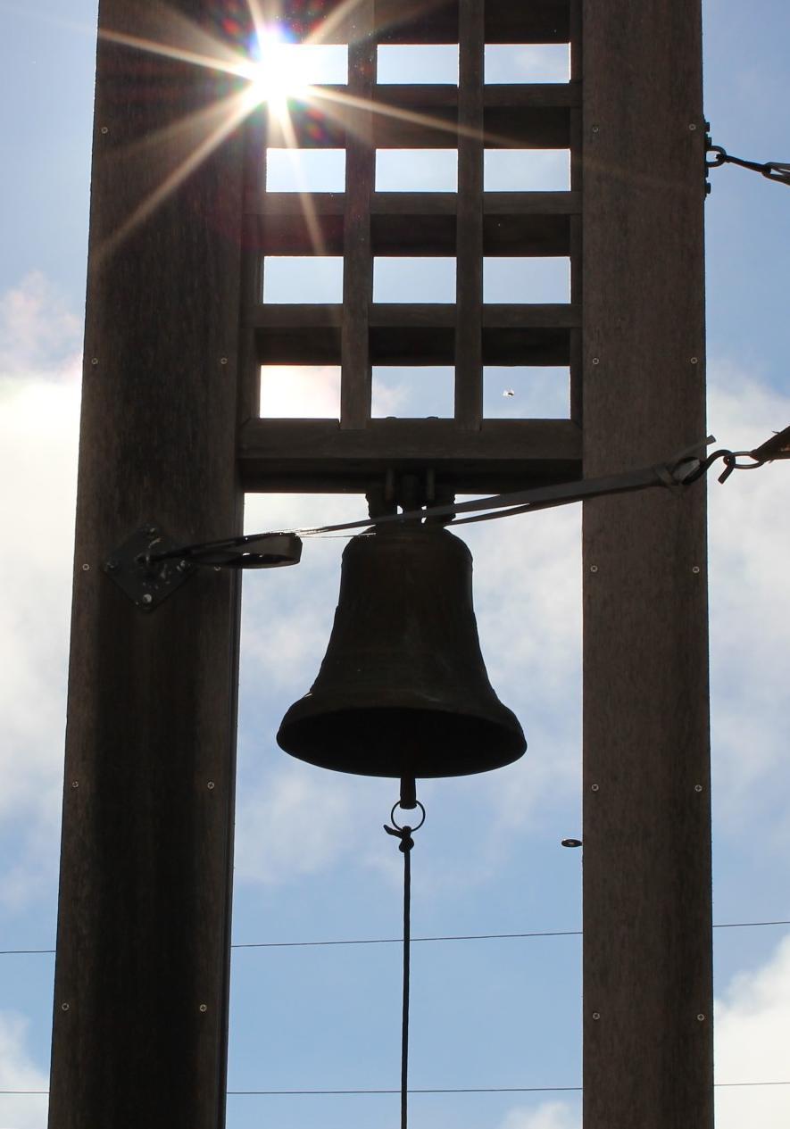 A bell hanging from a tall structure with a sunny sky background.