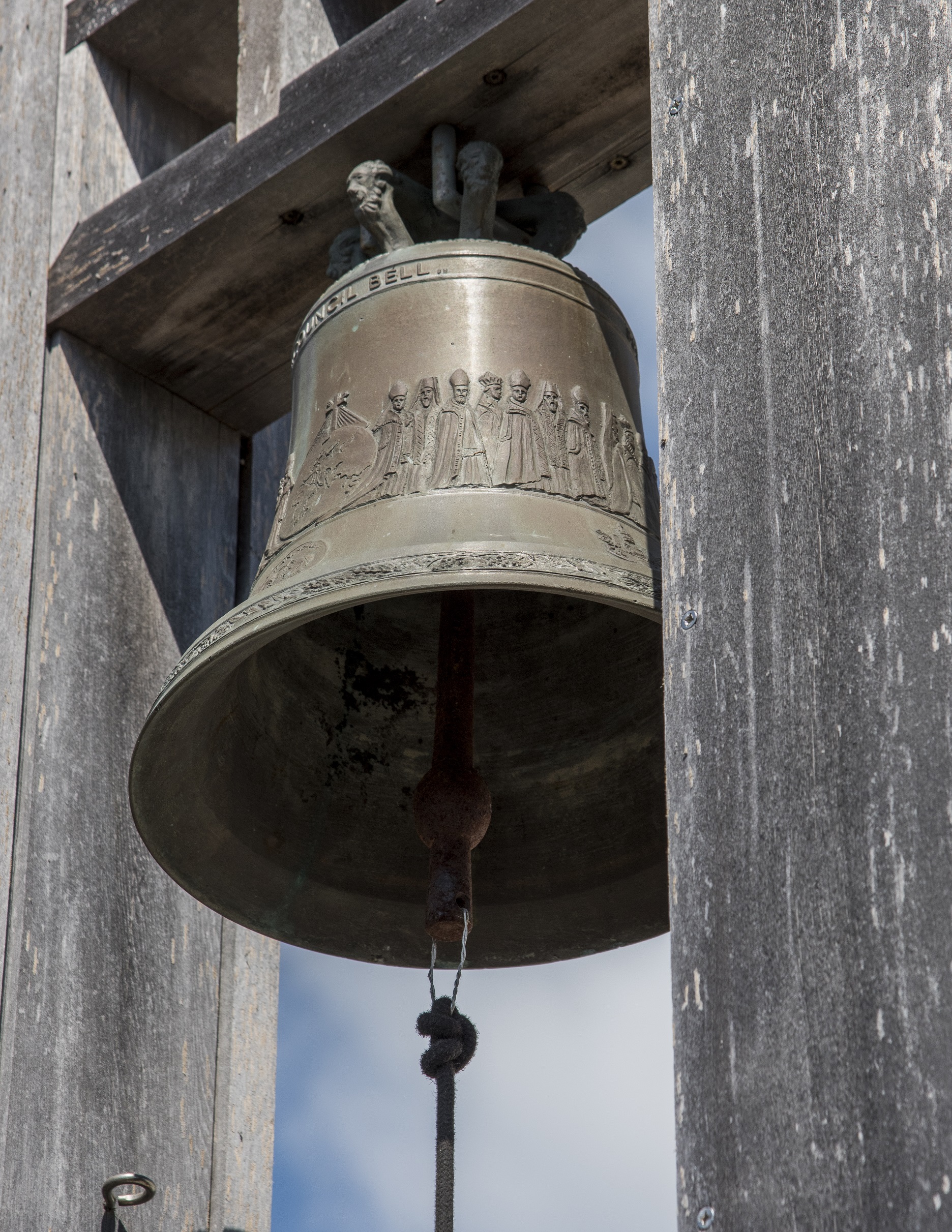 Bronze bell on a wooden bell tower against blue sky.