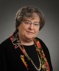 A person wearing glasses and a colorful scarf against a gray background.