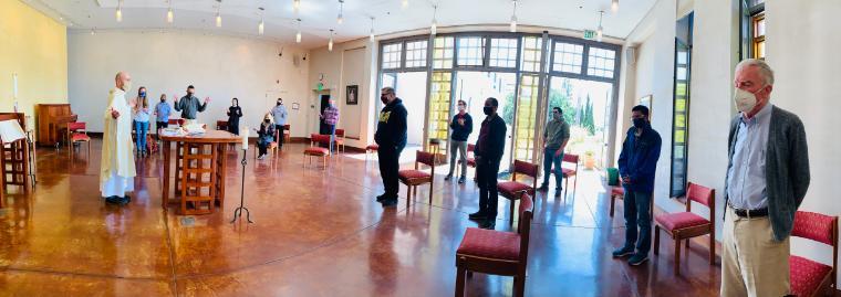 People attending the first JST in-person liturgy in a room with wooden floors.