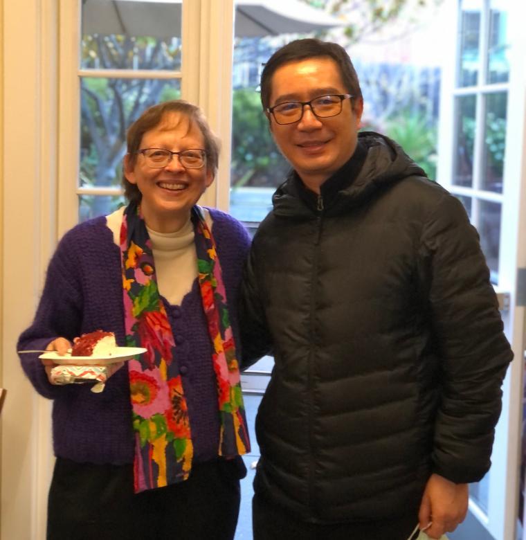 Two people smiling indoors, one holding a plate of food.