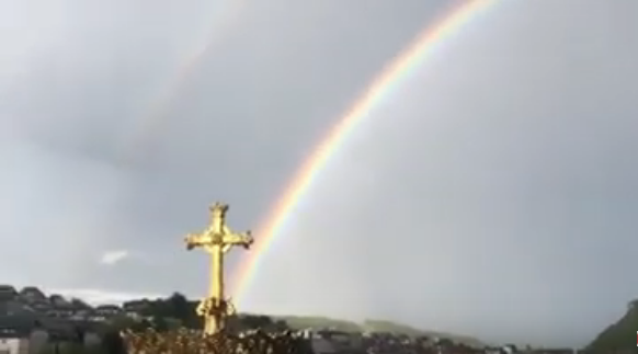 Double rainbow over Lourdes with a cross in the foreground.