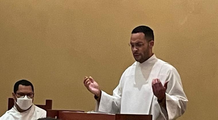 A preacher delivering a sermon next to a seated person.