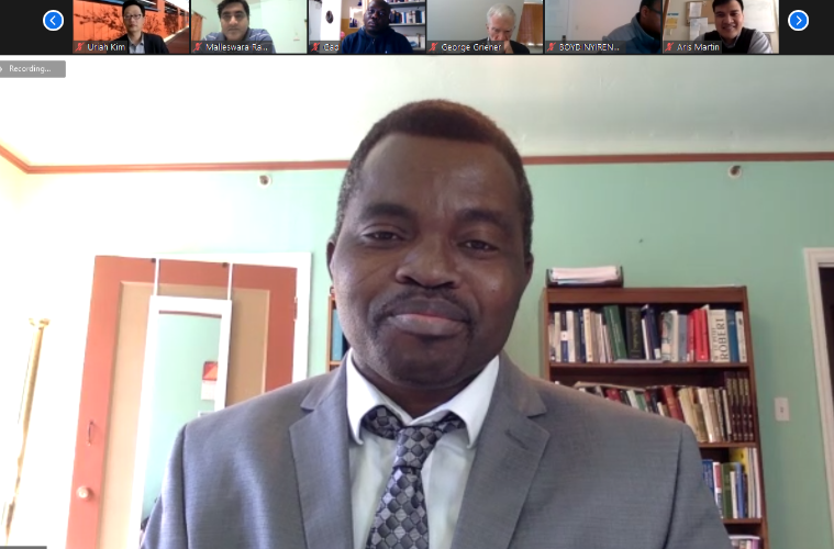 Alt text: Person in a suit on a video call during dissertation defense with participants' thumbnails at the top.