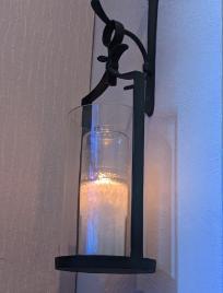 Lit candle in glass holder mounted on a wall with a metal bracket.