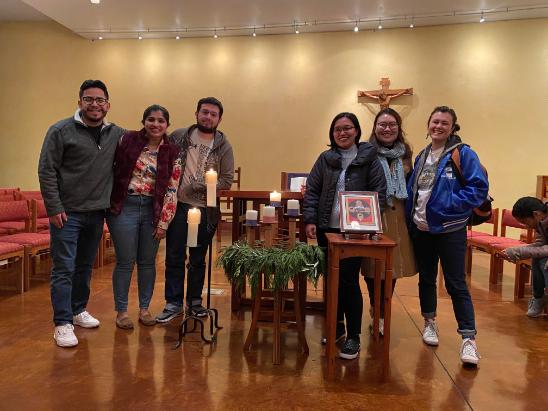 A group of people standing in a room with a cross.