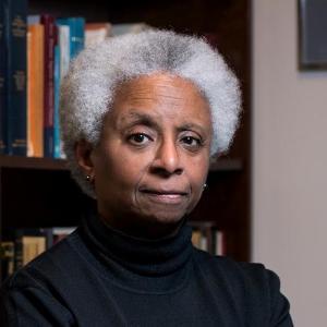 A person stands with arms crossed in front of bookshelves.