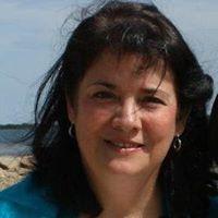 A person smiling outdoors with the sea in the background.
