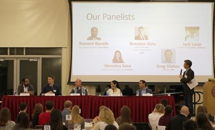 Panel discussion with presentation screen showing 'Actg Panel 2018' and audience watching.