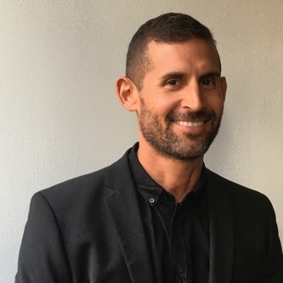 A person smiling in a black blazer against a plain background.