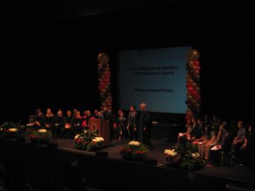 Large group on stage with lighting and a central screen displaying 