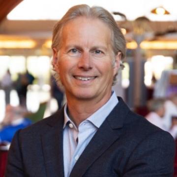 A person smiling and wearing a suit in an indoor setting.