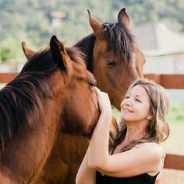 A person smiles while petting one of two horses.