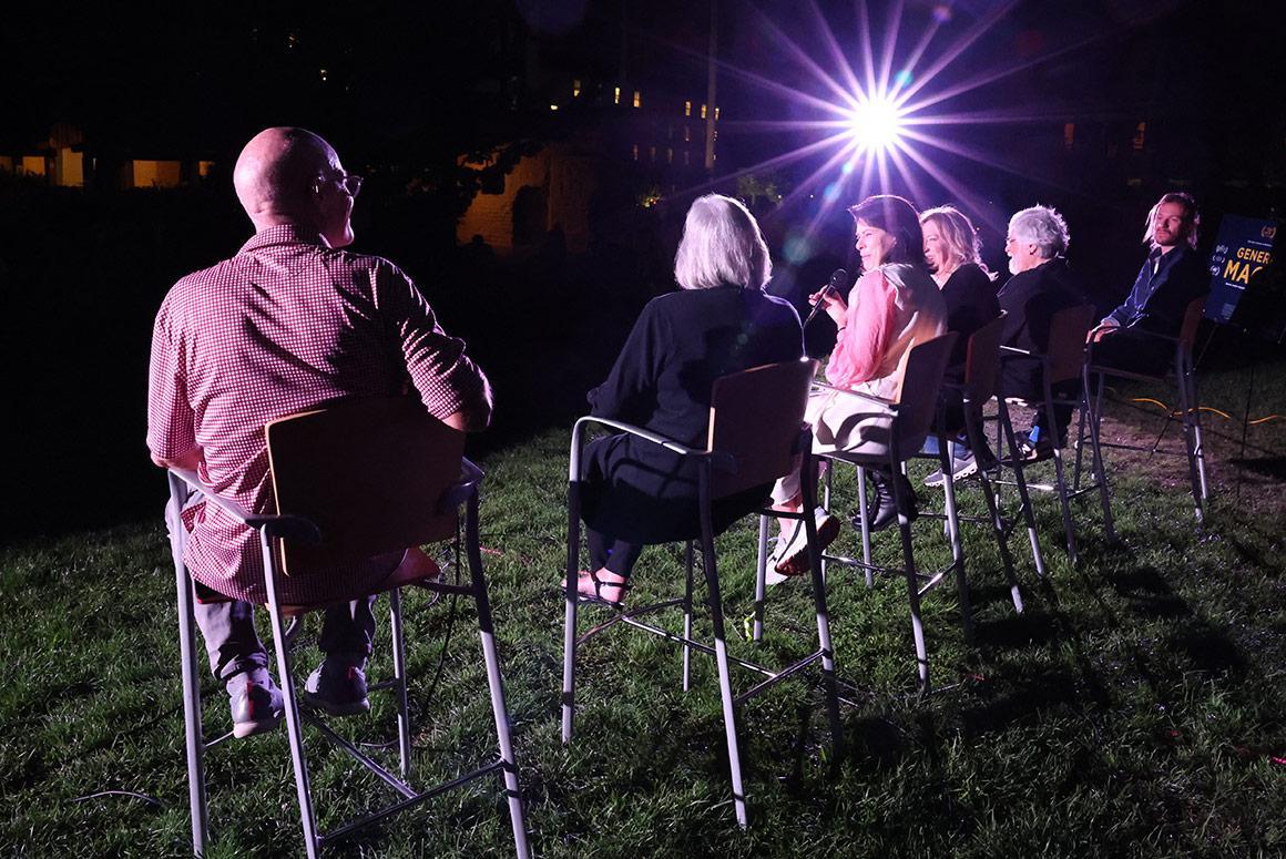 People sitting on lawn chairs outdoors under a bright light at night.