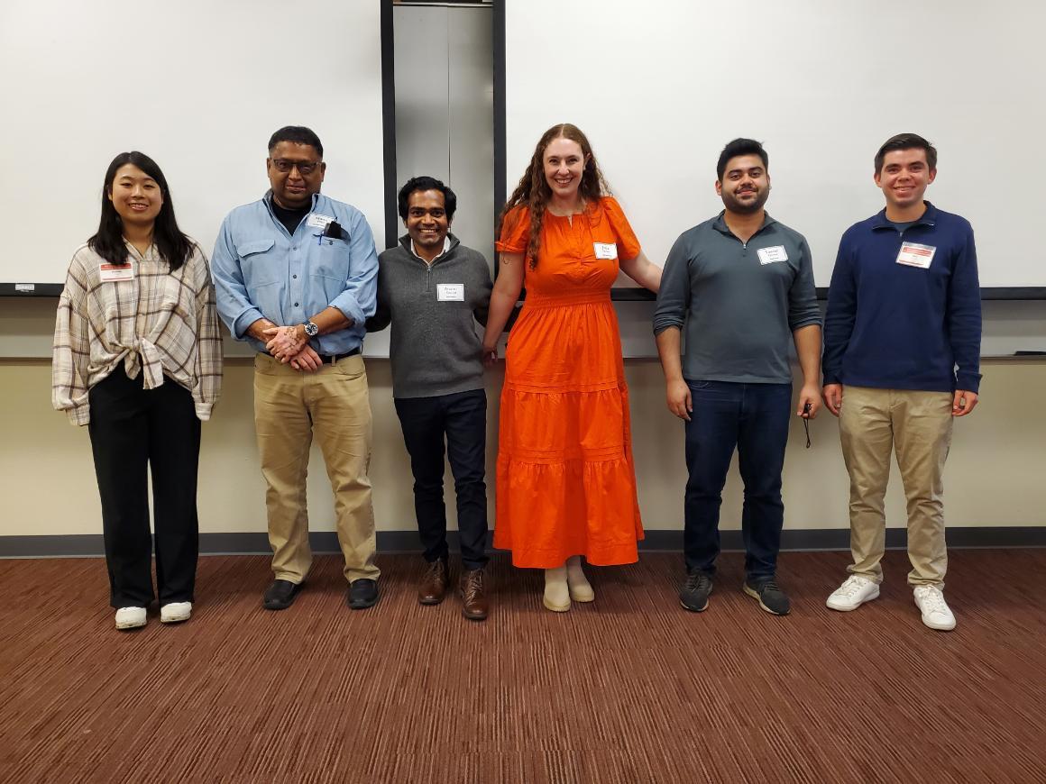 Six people standing side by side with name tags in a classroom.