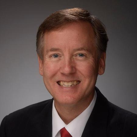 A smiling man in a suit and red tie.