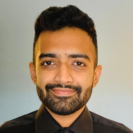 A man smiling in front of a plain background.