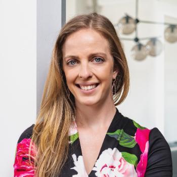 A person smiling with arms crossed in an indoor setting.