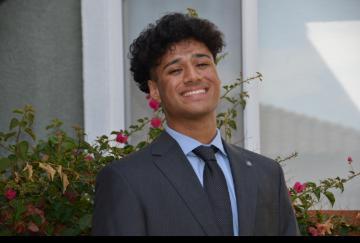 A person in a suit smiling in front of greenery.