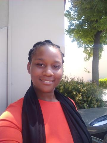 A person in an orange top and black scarf, smiling outdoors.